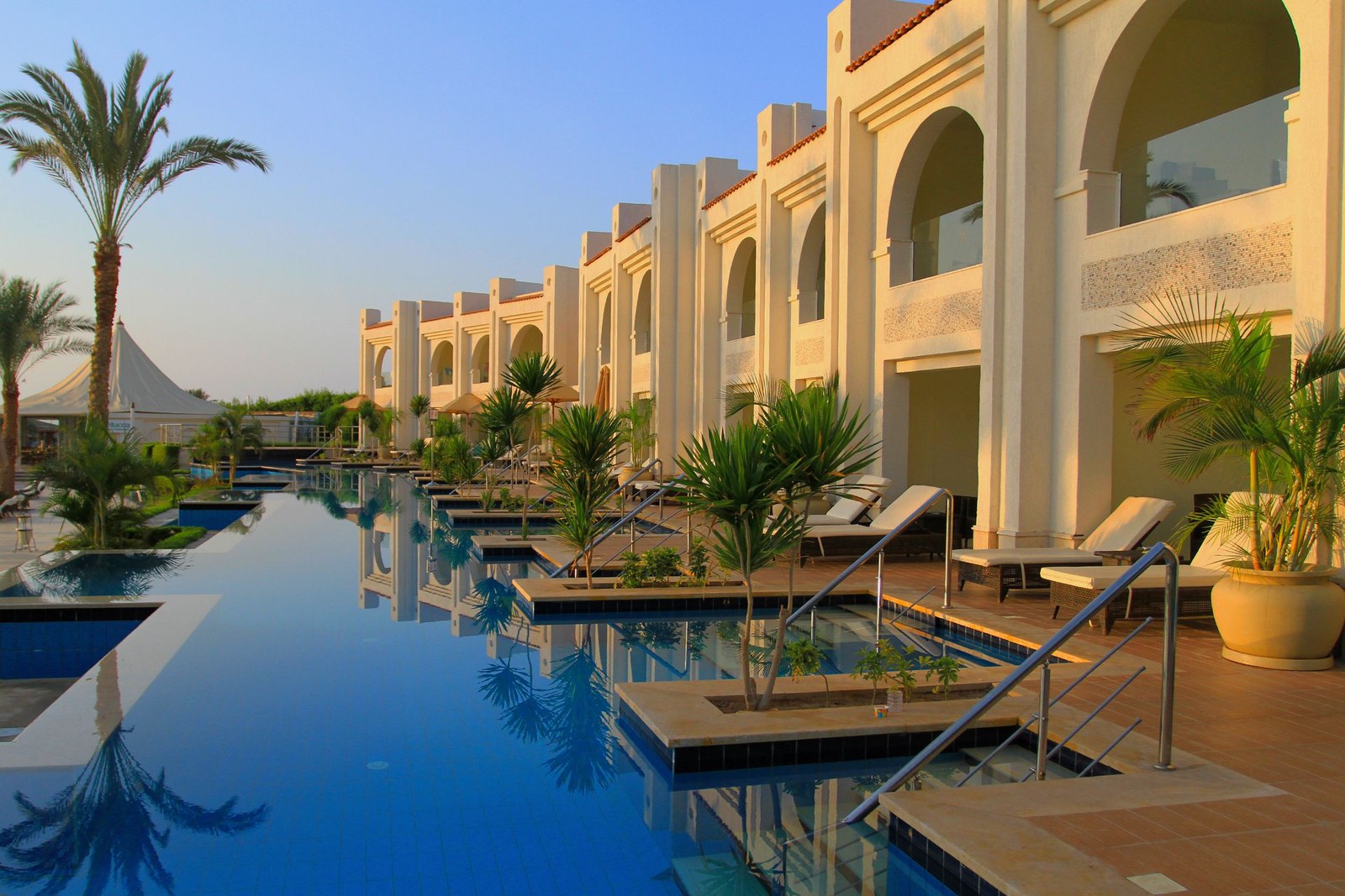 Sunlit luxury resort with an infinity pool lined with palms and lounge chairs